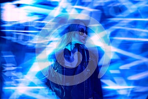 Portrait of young beautiful girl in leather jacket posing over blue background with abstract neon elements. Unfocused