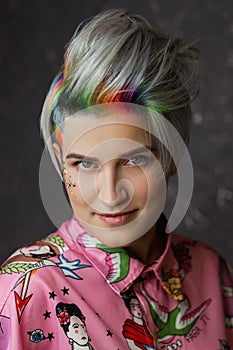 Portrait of a young beautiful girl in a pink shirt on a gray background with dyed hair. Short haircut pixie or bob