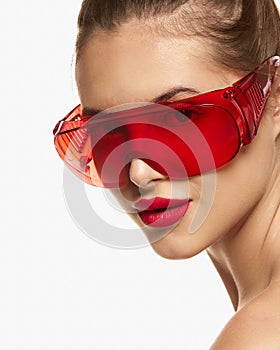 Portrait of young beautiful girl posing in red glasses isolated over white background. Laser cosmetology treatment