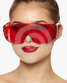 Portrait of young beautiful girl posing in red plastic glasses isolated over white background. Laser cosmetology