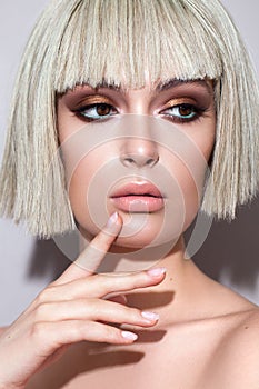 Portrait of a young beautiful girl with professional makeup, golden eyeshadow, mint eyeliner and a blond wig on her head