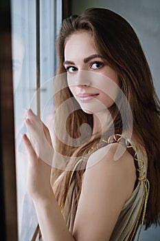 Portrait of a young beautiful girl standing near a window