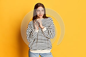 Portrait of young beautiful girl in striped sweater with plotting face posing against yellow studio background