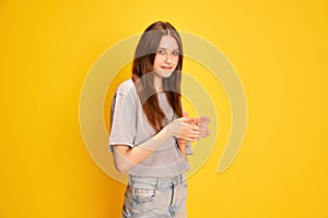 Portrait of young beautiful girl, student in casual clothes posing against yellow studio background. Smiling