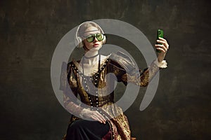 Portrait of young beautiful girl in vintage dress, trendy sunglasses and headphones, taking selfie with phone against