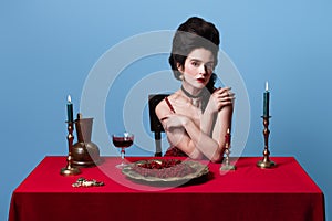 Portrait of young beautiful gorgeous woman in dark red, wine color evening dress posing isolated on blue background.