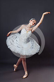 Portrait of young beautiful graceful caucasian ballerina practice ballet positions in tutu skirt of white swan from Swan Lake.