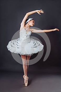 Portrait of young beautiful graceful caucasian ballerina practice ballet positions in tutu skirt of white swan from Swan Lake.