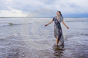 Portrait of young beautiful and happy Asian Chinese woman on her 20s or 30s wearing long chic dress walking alone on beach sea