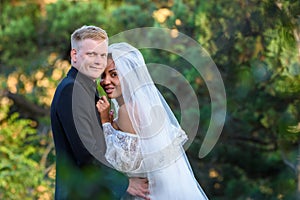 Portrait of young beautiful interracial newlyweds on green foliage background