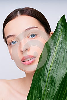 Portrait of a young beautiful lady with a green wet tropical leaf at the face