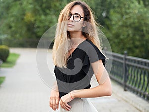 Portrait of young beautiful long hair woman wearing black blouse, holding mobile phone at summer green park path background.