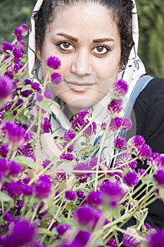 A portrait of a young beautiful muslim woman in a white shawl in front of purple flowers vertical shot