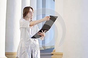 Portrait of a young nurse, a medical university student stands with a phonendoscope and reads a paper, happy female doctor in