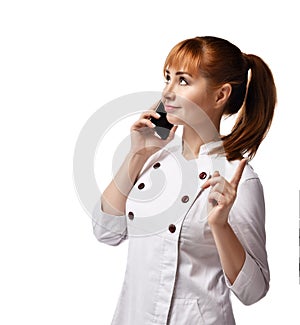 Portrait of young beautiful red-haired woman doctor or nurse in white special uniform standing and talking on phone