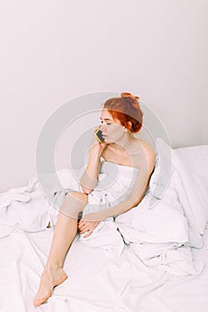 Portrait of a young beautiful redhead woman talking on the phone in bed