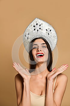 Portrait of young beautiful serious girl in nude dress and russian traditional hat kokoshnik, looking at camera