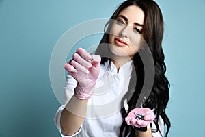 Portrait of young beautiful sexy brunette woman doctor or nurse in white costume and pink gloves holding accessories