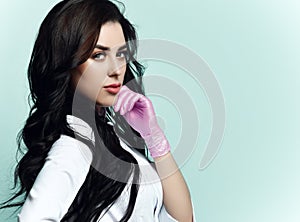 Portrait of young beautiful sexy brunette woman doctor or nurse in white costume and pink gloves over blue wall background