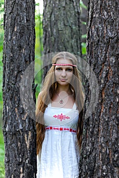 Portrait of a young beautiful Slavic girl with long hair and Slavic ethnic dress in a summer forest