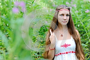 Portrait of a young beautiful Slavic girl with long hair and Slavic ethnic dress in thickets of tall grass