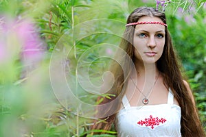 Portrait of a young beautiful Slavic girl with long hair and Slavic ethnic dress in thickets of tall grass