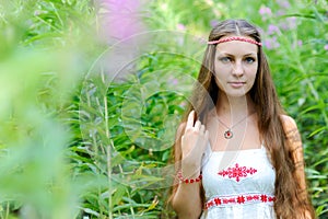 Portrait of a young beautiful Slavic girl with long hair and Slavic ethnic dress in thickets of tall grass