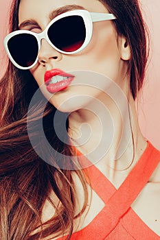 Portrait of young beautiful slim woman in sexy dress with sensual lips in studio wearing sunglasses. smiling and posing