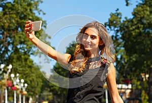 Portrait of young beautiful smiley woman making selfie outdoors