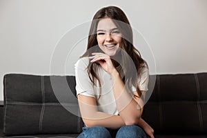 Portrait of young beautiful smiling brunette woman sitting on the sofa in her appartment holding hand near face looking happy,