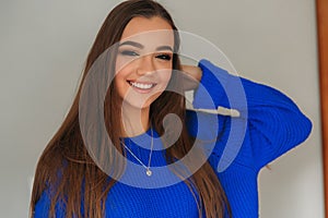 Portrait of the young beautiful smiling woman inside. Girl in bkue sweater. Fashion makeup