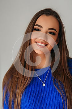 Portrait of the young beautiful smiling woman inside. Girl in bkue sweater. Fashion makeup