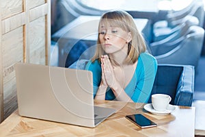 Portrait of young beautiful student with blonde hair in blue t-shirt sitting in cafe and talking thought webcame with group mate