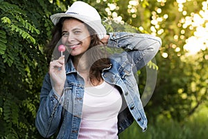 Portrait of young beautiful stylish girl in hat with sweet caramel candy chupa chups on stick on nature background photo