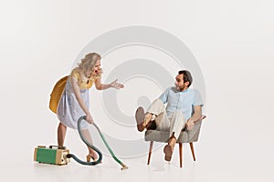 Portrait of young beautiful stylish woman shouting at man while cleaning with vacuum cleaner. Emotive family