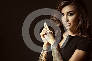 Portrait of young beautiful tattooed woman with luxuriant shining wavy hair and perfect make up holding hands in shooting gesture photo