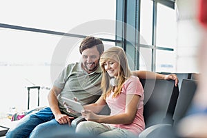 Portrait of young beautiful teenage girl showing digital tablet to her father while sitting and waiting for their flight in