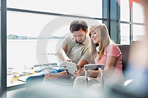 Portrait of young beautiful teenage girl showing digital tablet to her father while sitting and waiting for their flight in