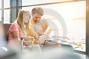 Portrait of young beautiful teenage girl showing digital tablet to her father while sitting and waiting for their flight in