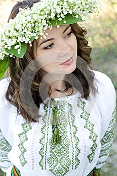 Portrait of a young beautiful in traditional Ukrainian embroidered shirt and a wreath of lilies of the valley