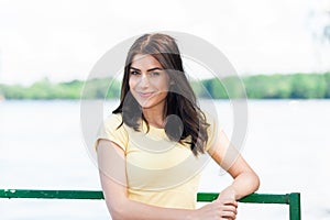 Portrait of young beautiful woman against lake in summer city park.