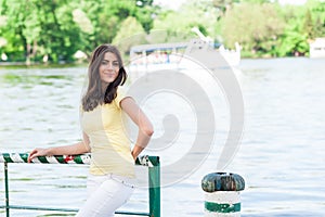 Portrait of young beautiful woman against lake in summer city park.