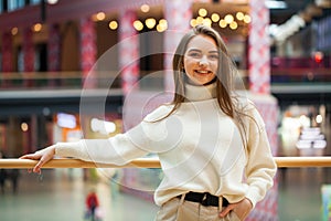 Portrait of a young beautiful woman in beige sweater and pants posing in the mall