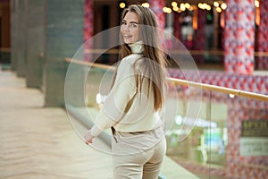 Portrait of a young beautiful woman in beige sweater and pants posing in the mall