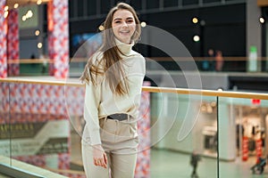 Portrait of a young beautiful woman in beige sweater and pants posing in the mall