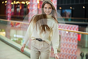 Portrait of a young beautiful woman in beige sweater and pants posing in the mall