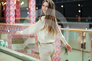 Portrait of a young beautiful woman in beige sweater and pants posing in the mall