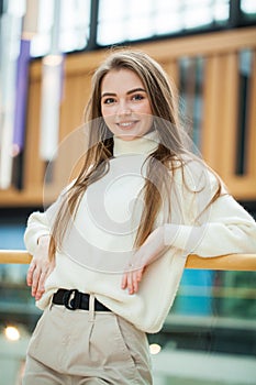 Portrait of a young beautiful woman in beige sweater and pants posing in the mall