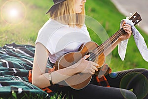 Portrait of a young beautiful woman in a black hat. Girl sitting on the grass and playing guitar
