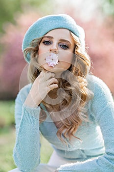 Portrait of young beautiful woman with blond hair wearing blue beret and holding flower in her mouth.
